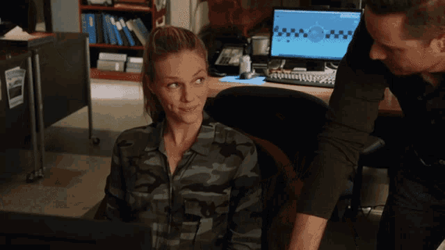 a woman in a camouflage shirt sits in front of a computer screen