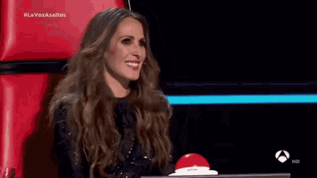 a woman is sitting in a red chair with her mouth open and a red button .