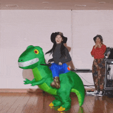 a woman is riding on the back of a green inflatable dinosaur