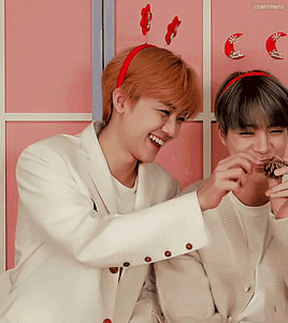 a man wearing a red headband laughs while another man holds a cookie in his mouth