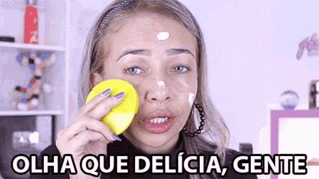 a woman cleaning her face with a yellow sponge with the words olha que delicia gente written below her