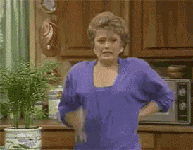 a woman in a purple shirt is standing in a kitchen holding a tissue .