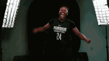 a woman wearing a purdue basketball jersey is jumping in the air with her arms outstretched