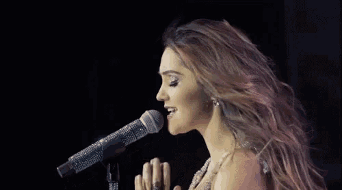 a woman is singing into a microphone with her hand in the air