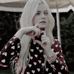 a woman in a heart printed shirt is making a heart shape with her hands .