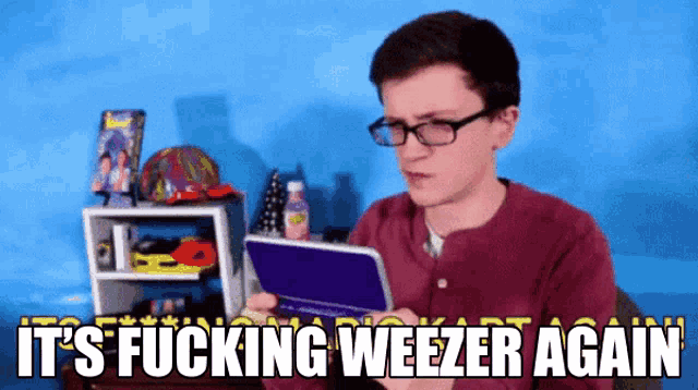 a man wearing glasses is playing a video game with the words it 's fucking weezer again