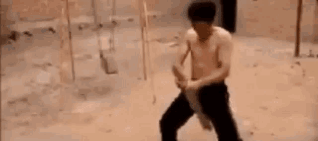 a man without a shirt is standing in a room with a sword in his hand .