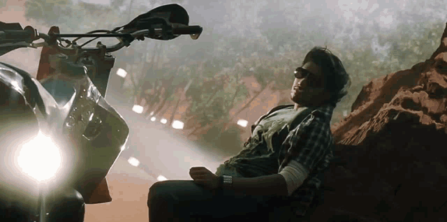 a man wearing sunglasses is sitting on a rock next to a motorcycle