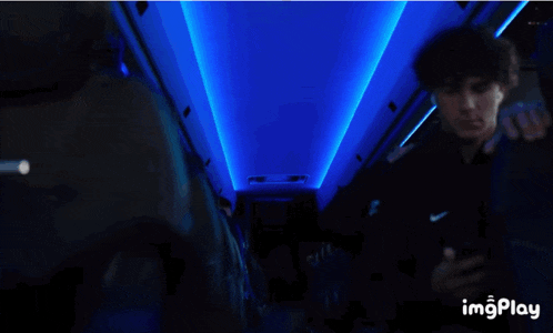 a man wearing headphones is smiling while another man looks at his phone in a dark room