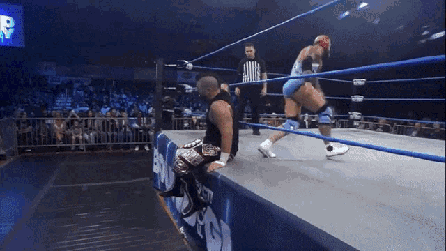 two wrestlers are in a ring with a referee and a sign that says r on it