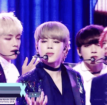 a group of young men singing into microphones on a stage with a blue curtain behind them