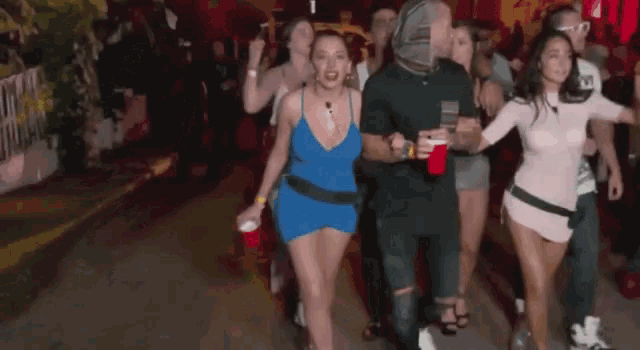 a group of people are walking down a street with a man holding a red cup