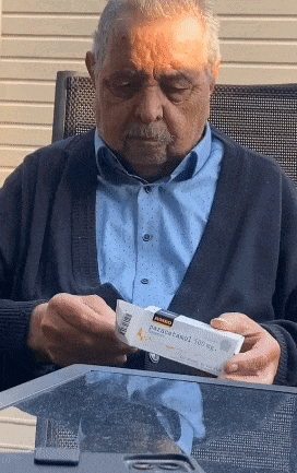 an elderly man sitting at a table looking at a box of paracetamol