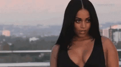 a woman in a black tank top is standing on a balcony with a city in the background .