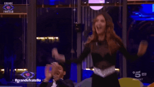 a woman is dancing in front of a sign that says #grandefratello