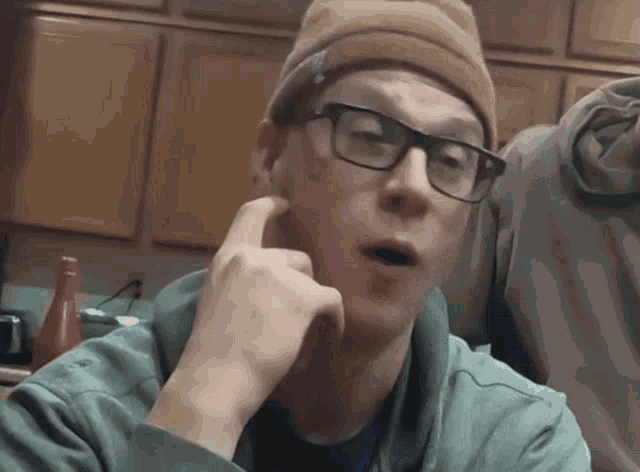 a man wearing glasses and a beanie holds his hand to his face