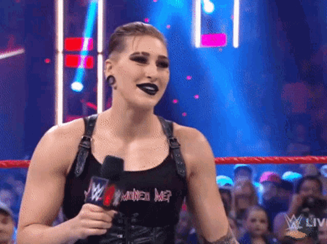 a woman is holding a microphone and wearing a tank top that says ' mine ' on it