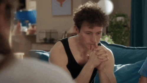 a man in a black tank top is sitting on a blue couch with his hands folded