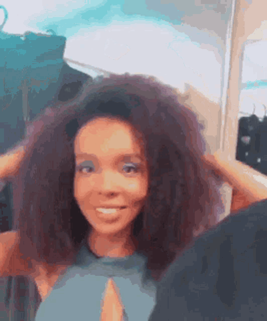 a woman with curly hair is smiling and holding her hair in her hands .
