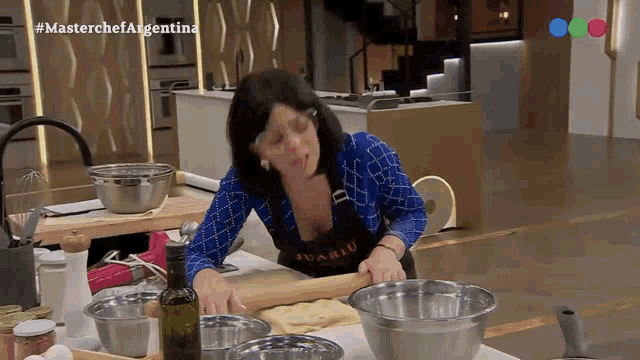 a woman is rolling out dough in a kitchen with a bottle of olive oil in front of her