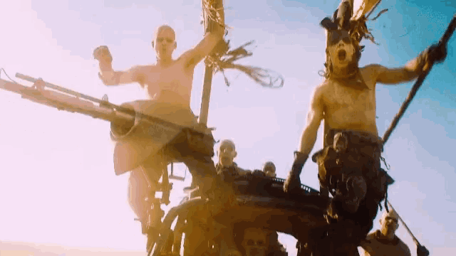a group of men are riding on the back of a vehicle with guns .