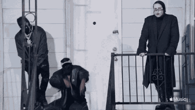 a man in a black coat is standing on a balcony next to two other people