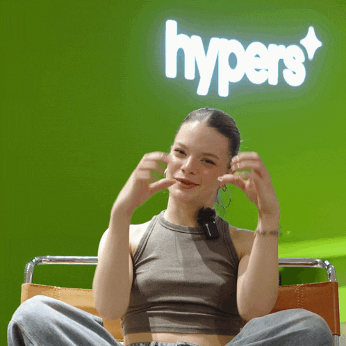a woman sitting in front of a green wall with the word hypers on it