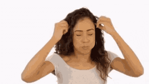 a woman is scratching her head with her hands while wearing a white shirt .