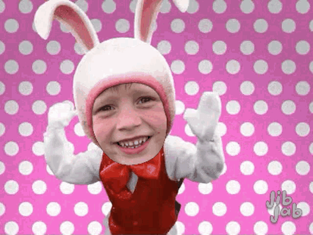 a child is wearing a bunny costume and smiling on a pink polka dot background
