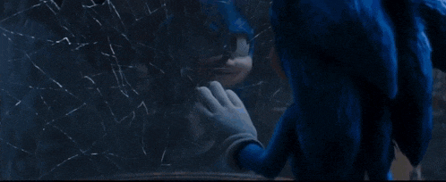 sonic the hedgehog is standing in front of a window with a reflection of a person in it .