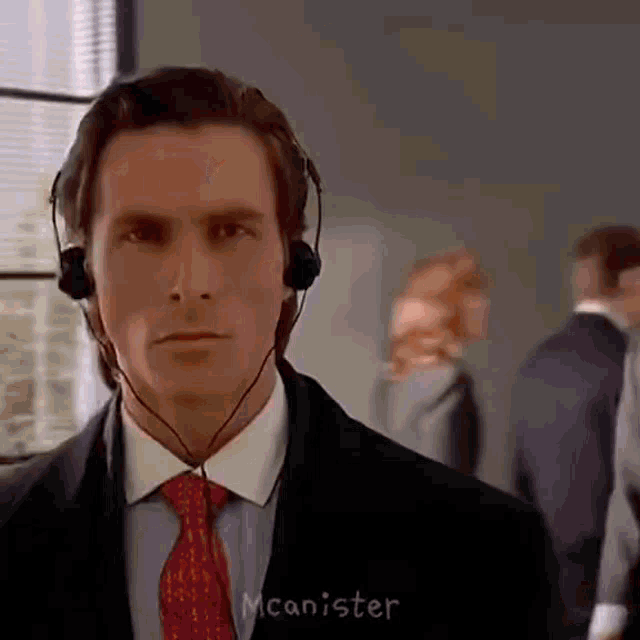 a man in a suit and tie is wearing a headset and the name mcanister is on the bottom right