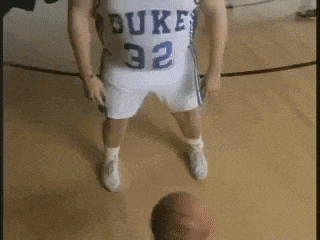 a man in a dukes jersey is standing on a basketball court