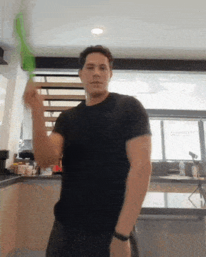 a man in a black shirt is holding a green spoon in his hand
