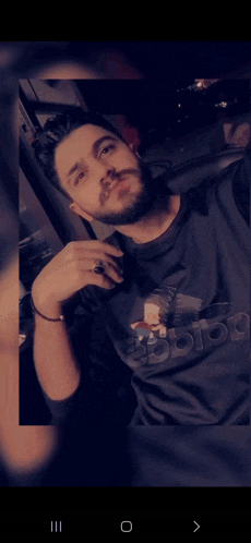 a man with a beard wearing an adidas shirt takes a selfie