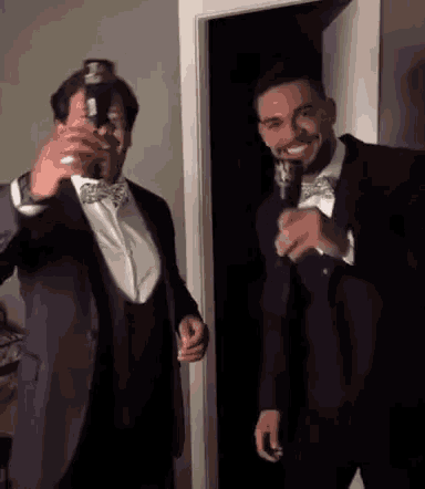 two men in suits and bow ties are standing in a doorway holding bottles of beer