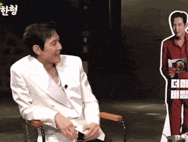 a man in a white jacket sits in front of a cardboard cutout of another man