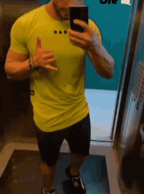 a man is taking a selfie in an elevator while wearing a neon yellow shirt and black shorts .