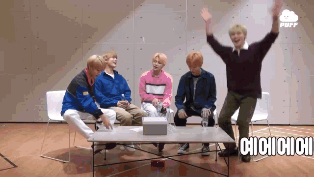 a group of young men are sitting around a table and one of them is raising his hand in the air .