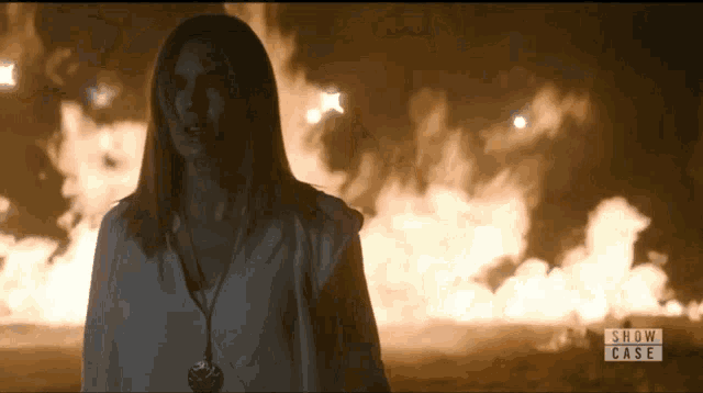 a woman stands in front of a fire with the words show case visible