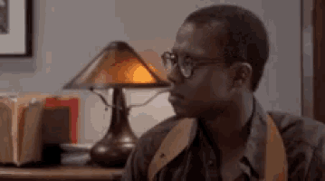 a man wearing glasses is sitting at a desk in front of a lamp .