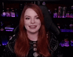 a woman with red hair is smiling while sitting in a chair in front of a shelf of potions .