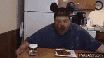 a man wearing a mickey mouse hat is sitting at a table with a jar of nutella .