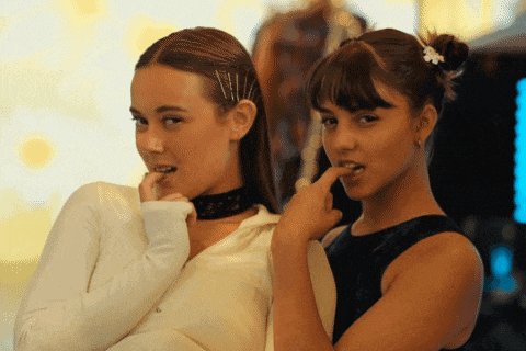 two women are standing next to each other and one of them is licking her finger