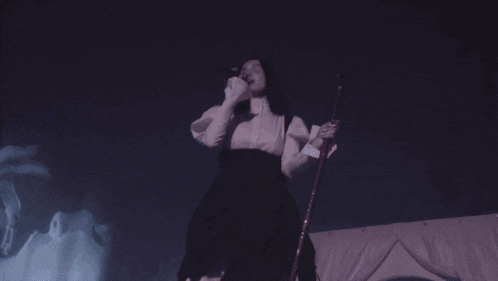 a woman singing into a microphone while holding a staff