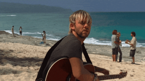 a man playing a guitar on a beach with people playing instruments in the background