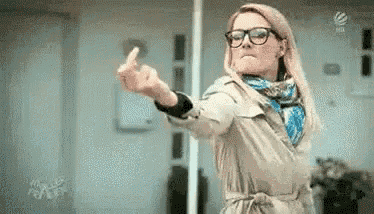 the woman is wearing glasses and a trench coat and is giving the middle finger .