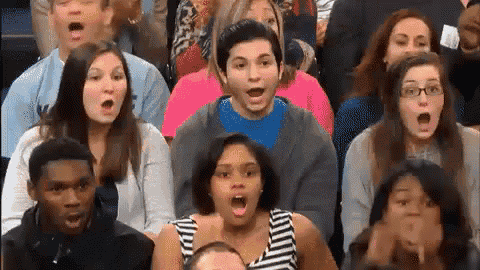 a group of people are sitting in a stadium with their mouths open and their faces surprised .