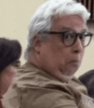 a man with white hair and glasses is making a funny face while sitting in a chair .