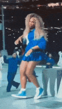 a woman in a blue dress is dancing in front of a crowd of people