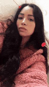 a woman with long black hair is wearing a pink sweater and has two red hearts in her hair